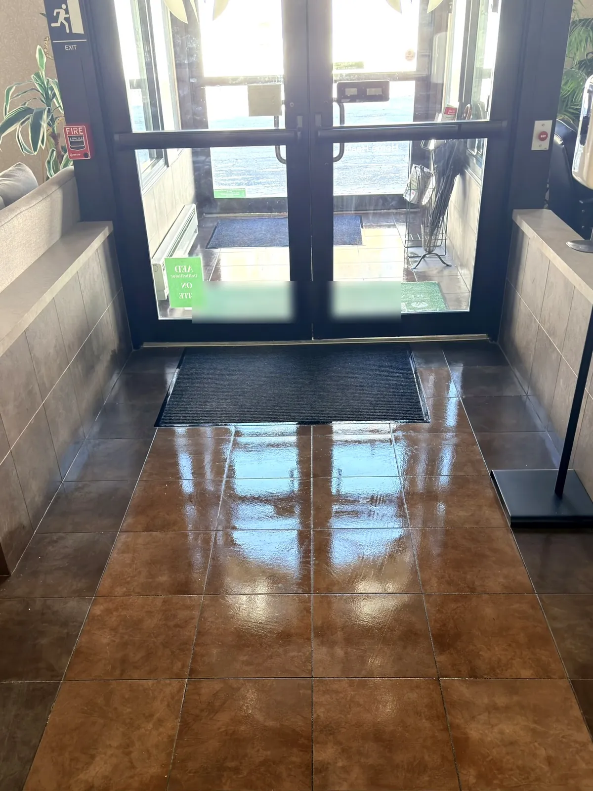 A commercial building entrance seen from inside: freshly cleaned tile floor reflecting the daylight from the glass doors